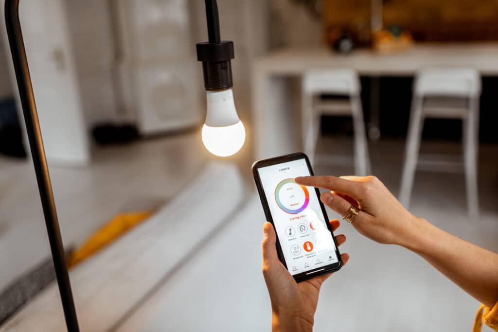 Contrôle lumière connectée : réglage couleur via smartphone Main d'une personne ajustant la couleur de l'ampoule connectée via l'application "LIGHTS" sur un smartphone.