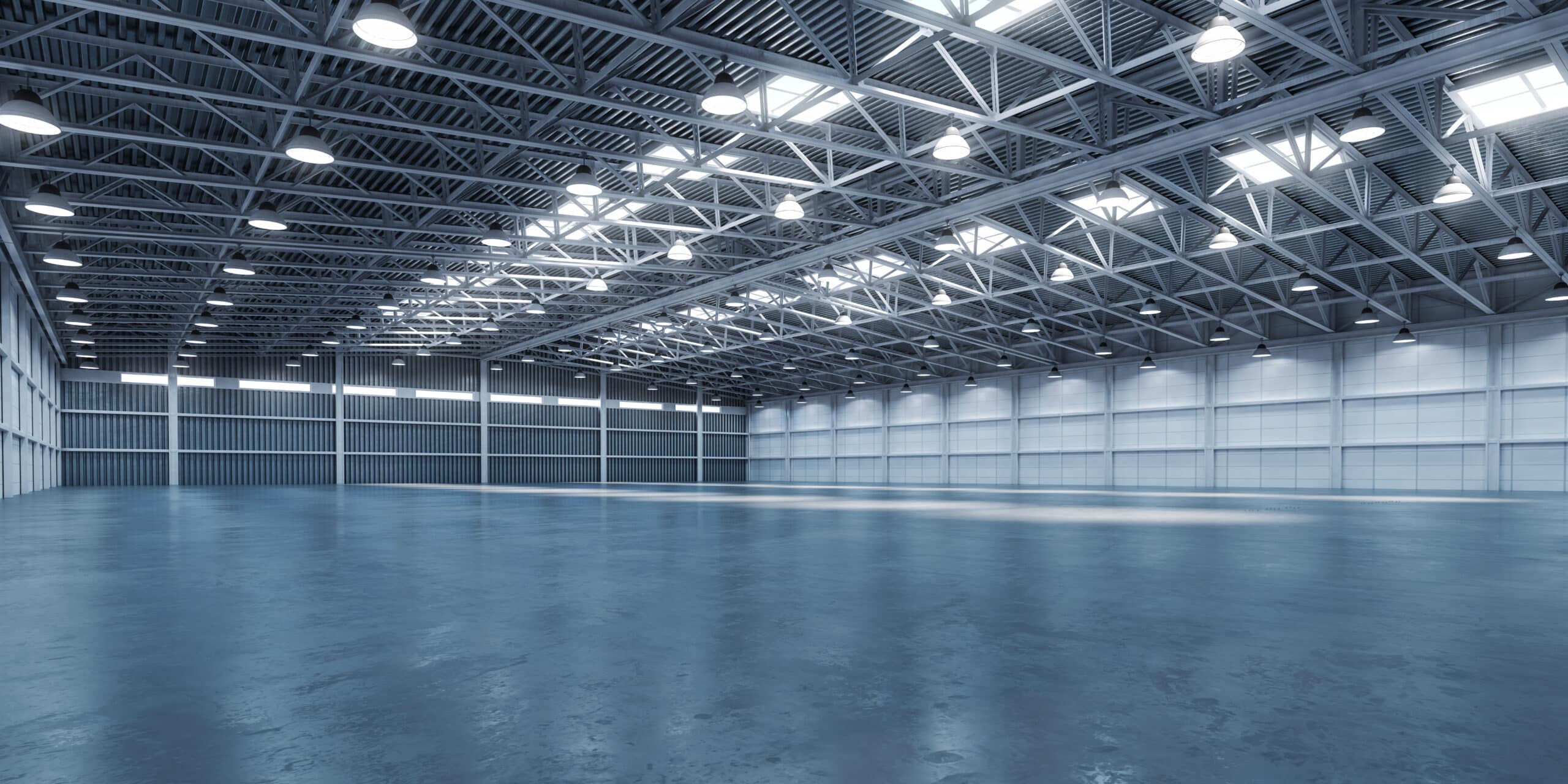 Intérieur vide d'un vaste entrepôt industriel moderne avec sol poli, murs modulaires clairs et haut plafond en treillis métallique éclairé par des suspensions et des puits de lumière.